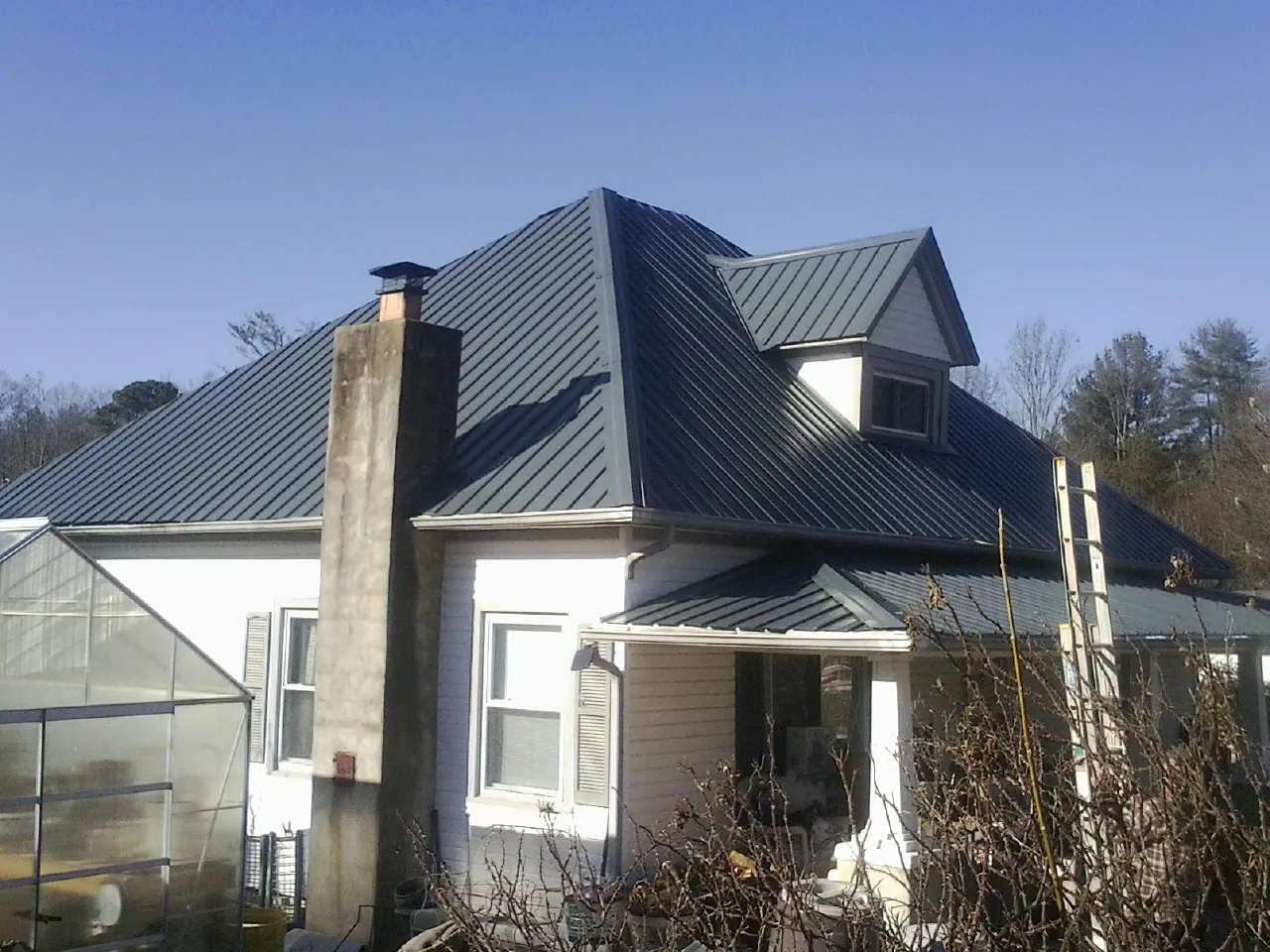 Dark blue standing seam metal roof on a white farmhouse with dormer — Slate & Tile Roof Repair by Roofing Brothers in Clyde Park