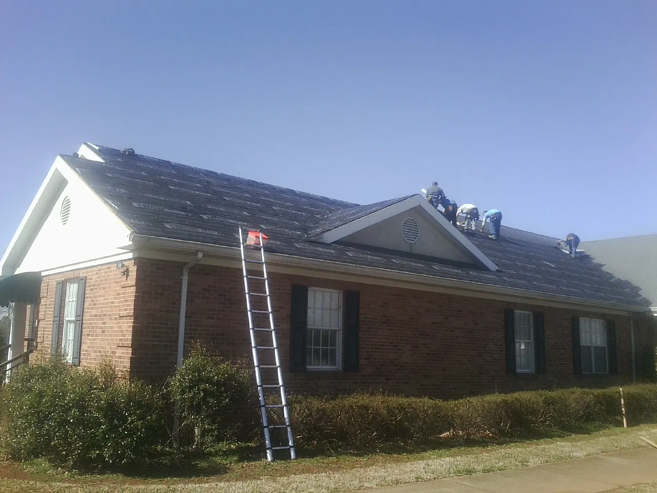 Crew tearing shingles off a brick ranch roof with a ladder set — Emergency Roof Repair work by our crew in Clyde Park