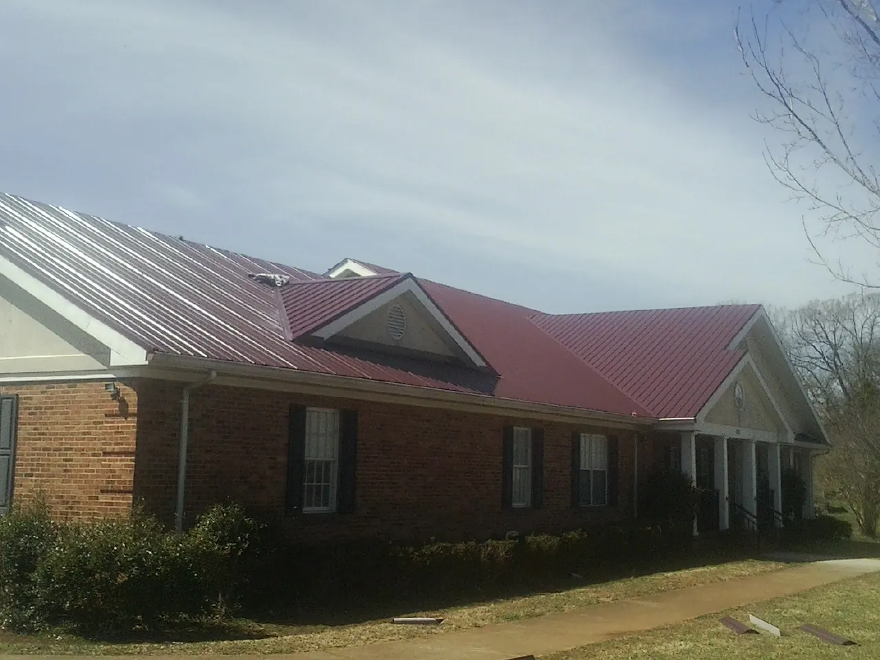 Red metal roof with gabled entries on a long brick building, from a Hail Damage Roof Repair job in Clyde Park