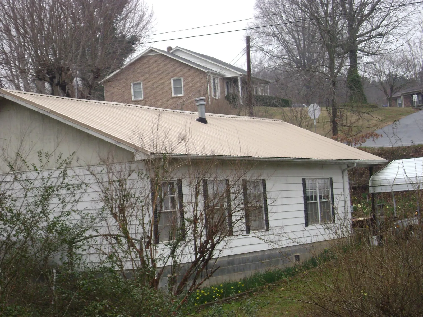 Tan metal roof on a white sided house set into a hillside — Commercial Roofing by Roofing Brothers in Clyde Park